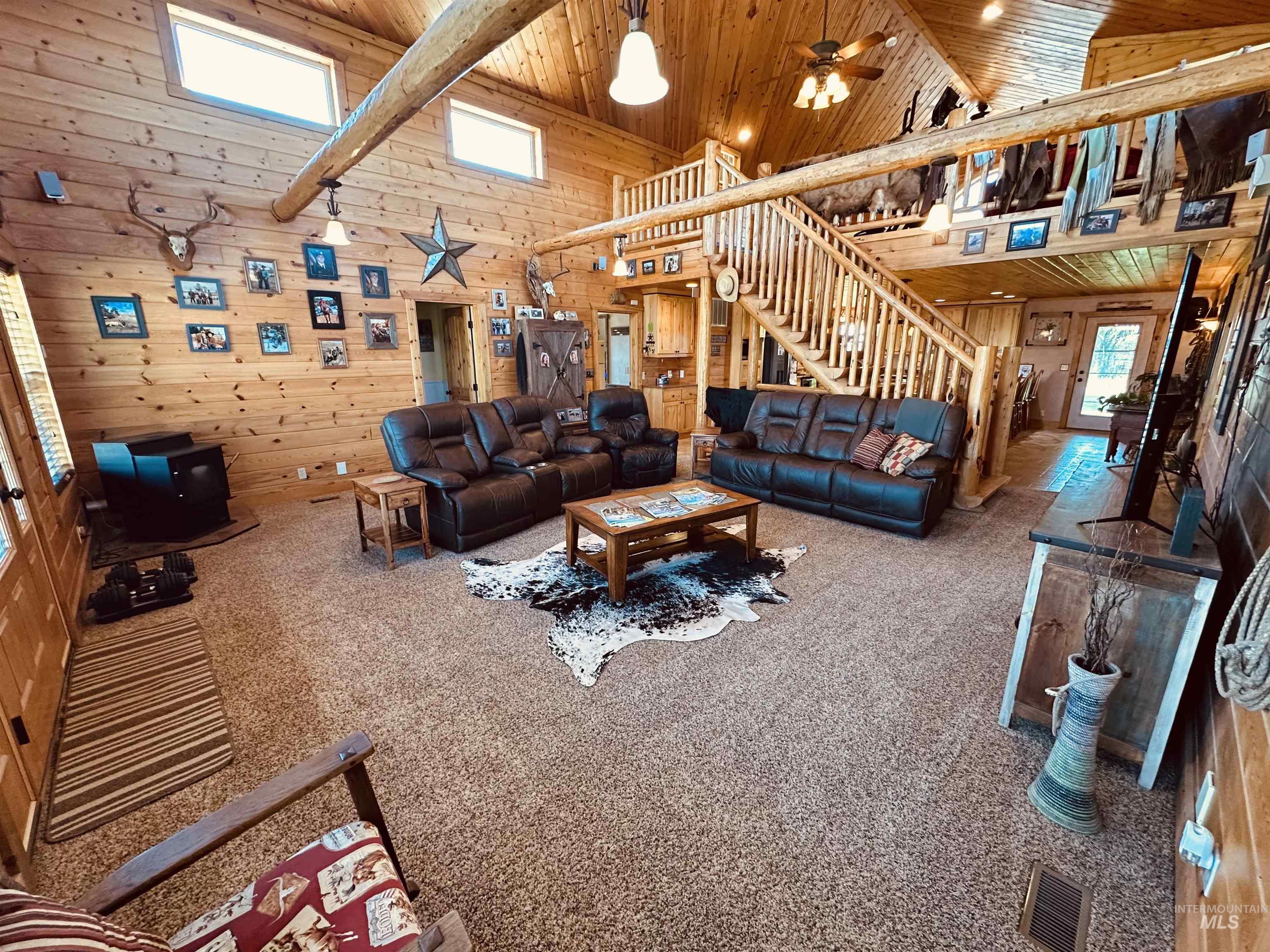 Living area with high vaulted ceiling, a wooden ceiling with exposed beams, stairs, wood walls, and carpet flooring