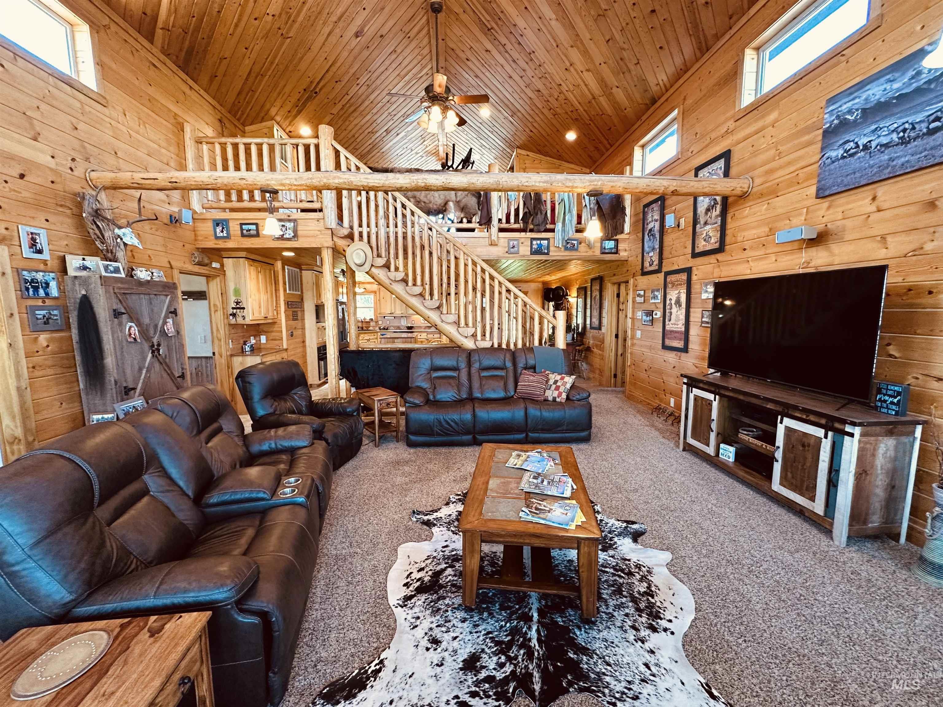 Carpeted living room with high vaulted ceiling, wooden walls, plenty of natural light, wood ceiling, and a ceiling fan