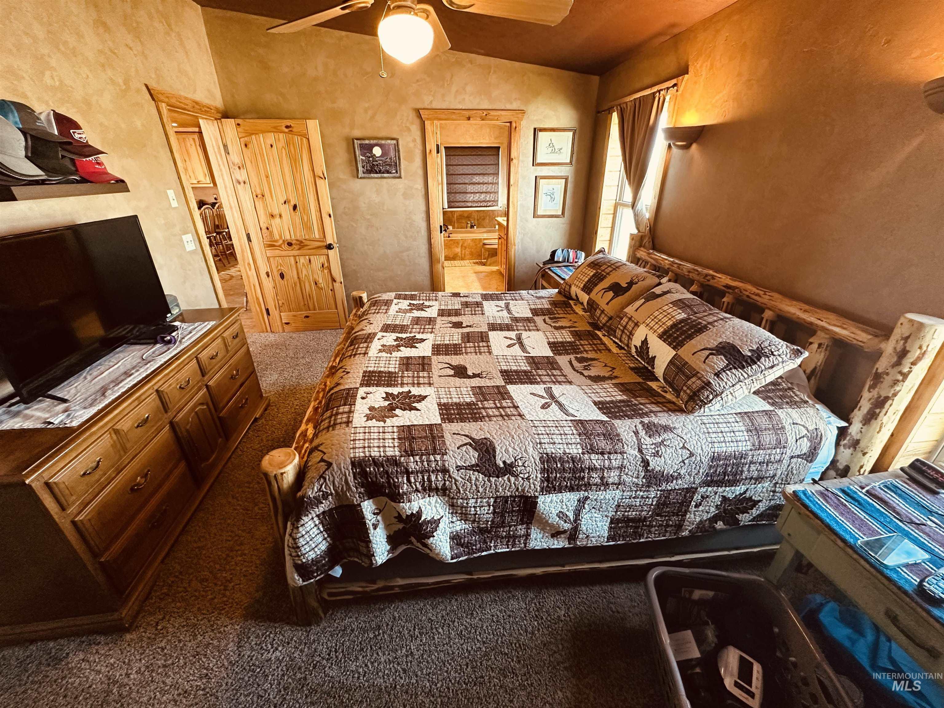 Bedroom with carpet, a textured wall, ensuite bathroom, vaulted ceiling, and ceiling fan