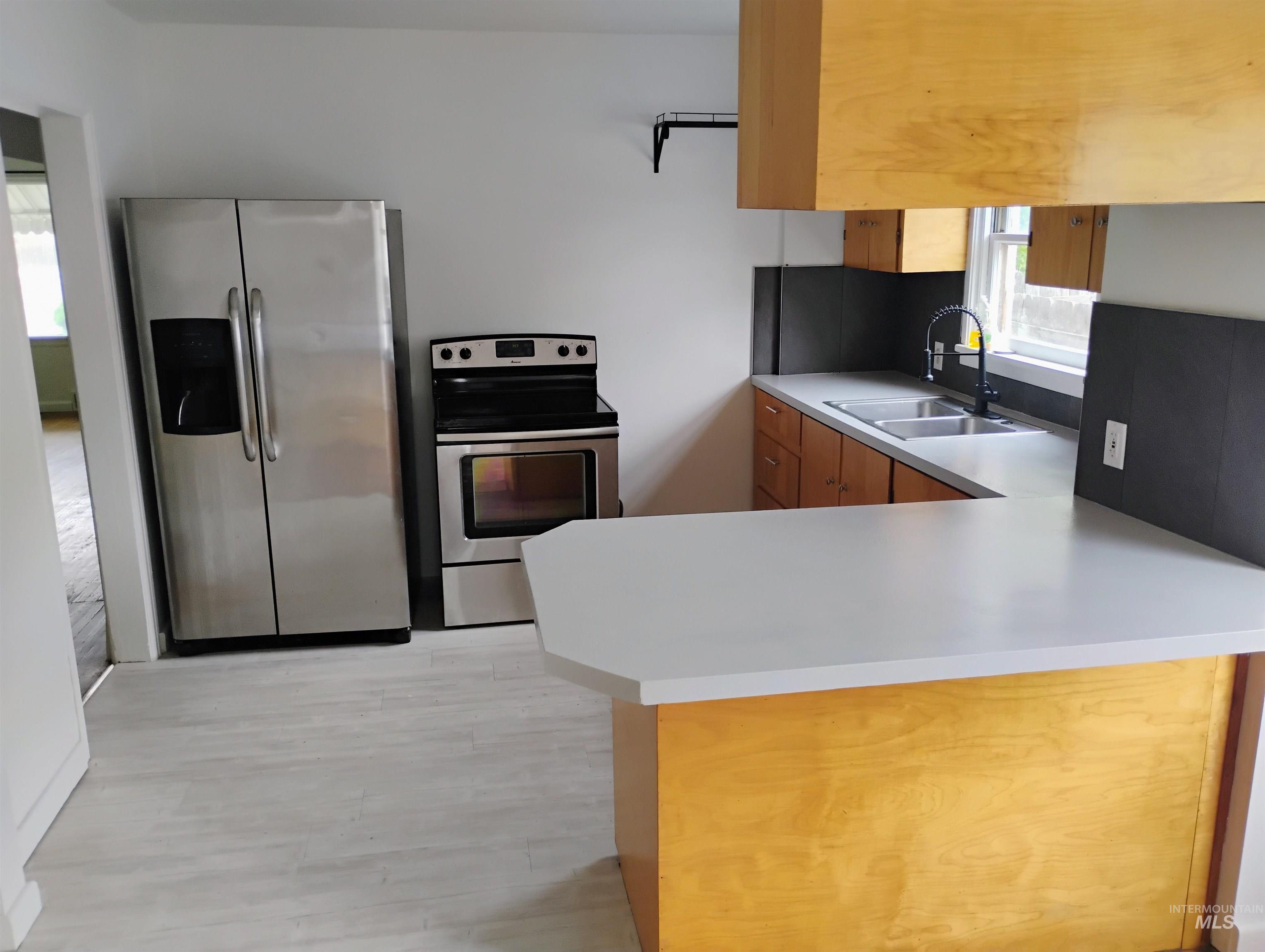 Kitchen with appliances with stainless steel finishes, a peninsula, light countertops, light wood-style floors, and brown cabinets