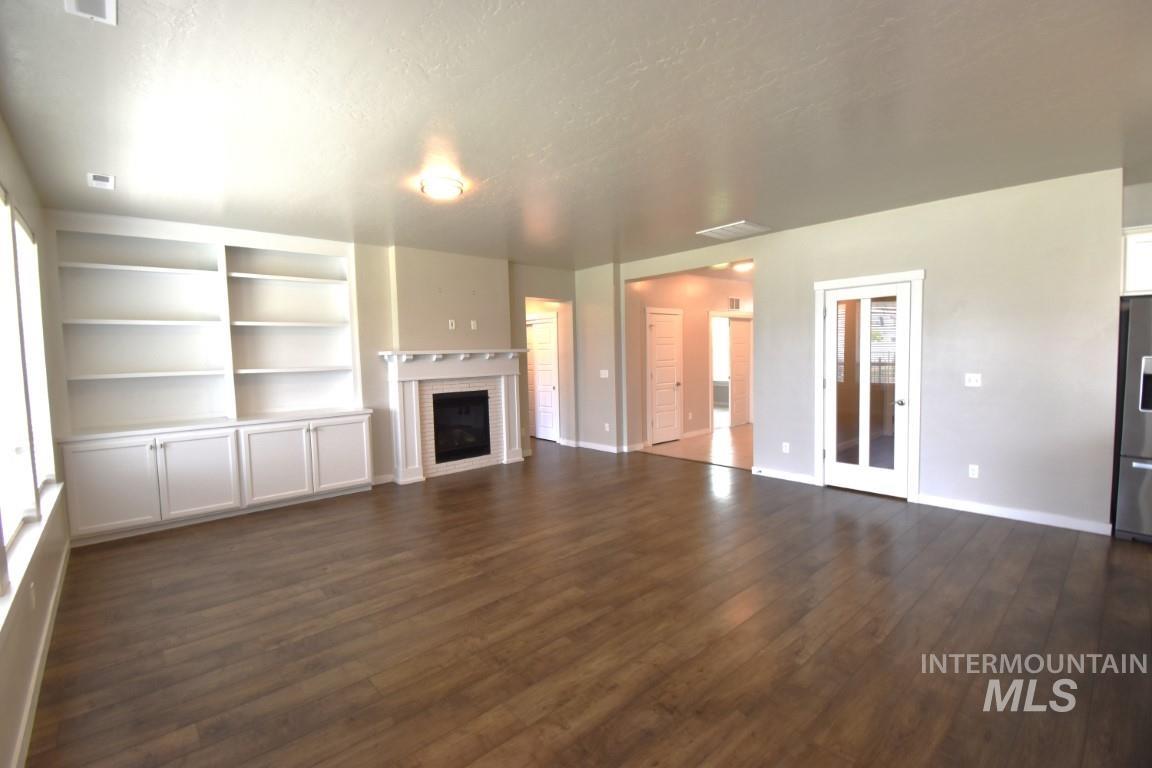 Unfurnished living room featuring dark wood-type flooring and a brick fireplace