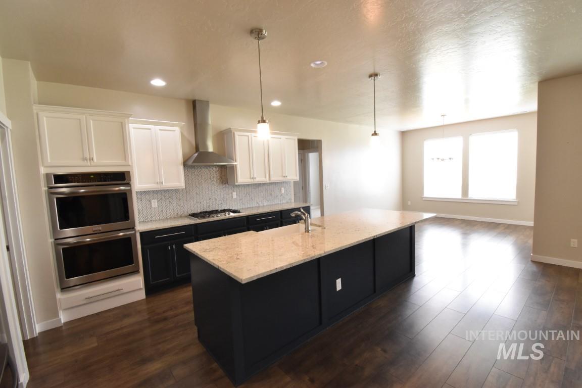 Kitchen with stainless steel appliances, white cabinetry, wall chimney exhaust hood, light stone counters, and backsplash