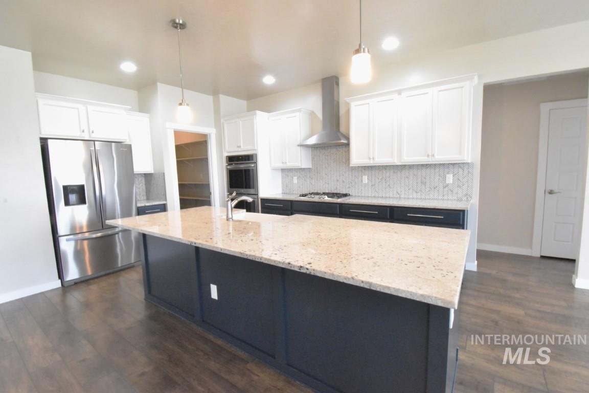 Kitchen with appliances with stainless steel finishes, tasteful backsplash, wall chimney range hood, white cabinets, and a center island with sink