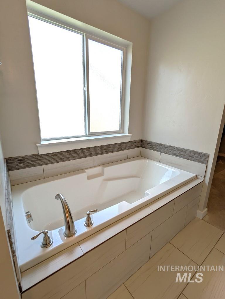 Full bath featuring healthy amount of natural light, a bath, and tile patterned flooring