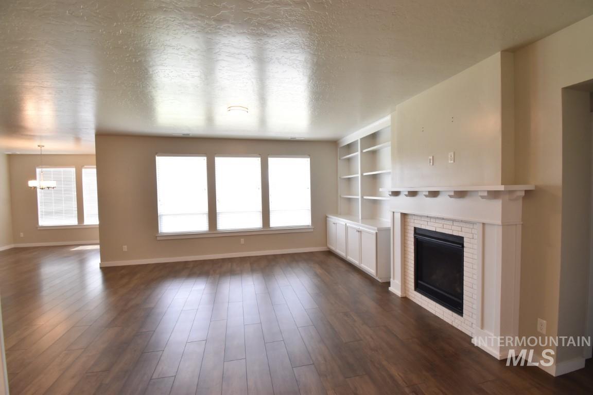 Unfurnished living room featuring a brick fireplace, a chandelier, dark wood-style floors, a textured ceiling, and built in features