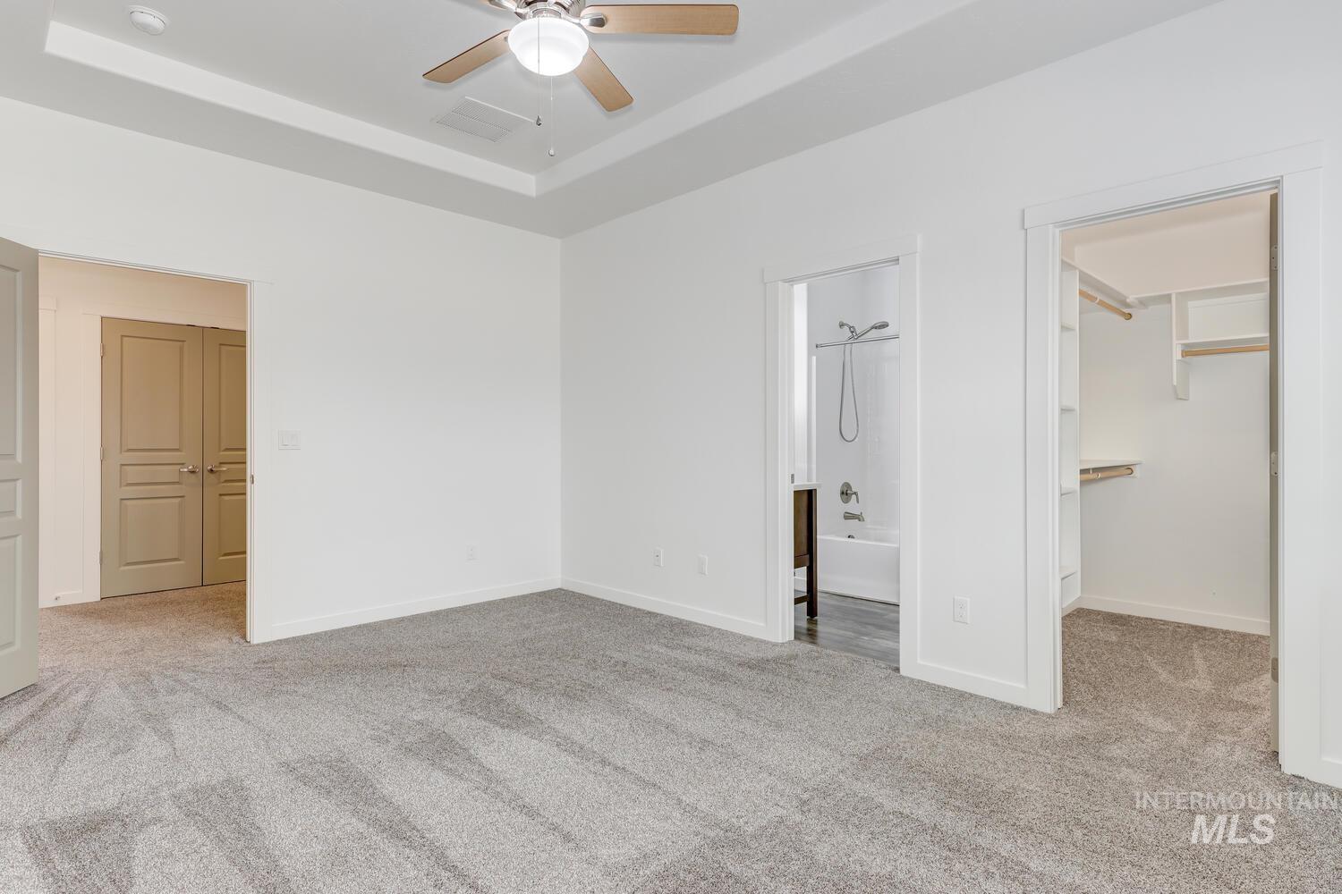 Unfurnished bedroom featuring carpet floors, a spacious closet, a tray ceiling, and connected bathroom
