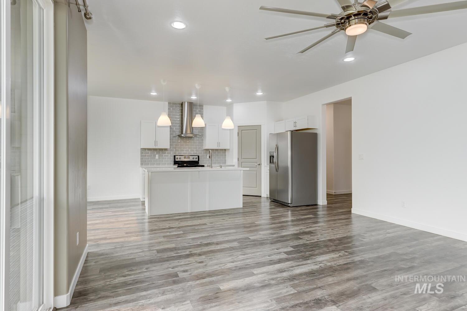 Kitchen with open floor plan, stainless steel fridge, wood finished floors, wall chimney exhaust hood, and light countertops