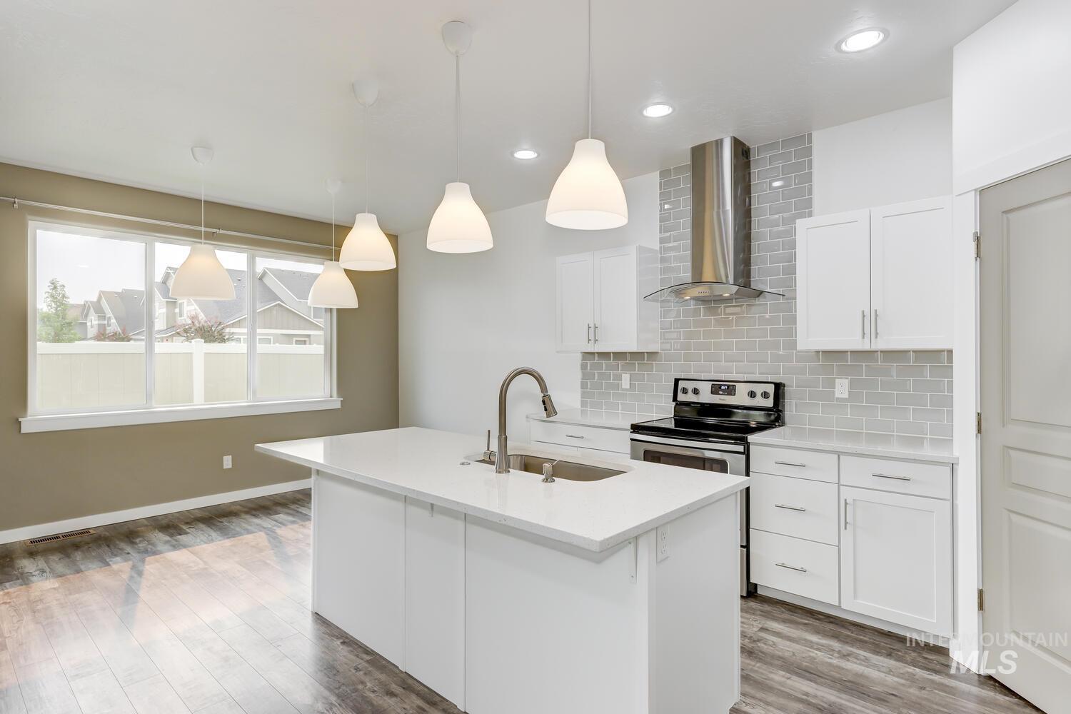 Kitchen featuring decorative backsplash, wall chimney exhaust hood, white cabinetry, a kitchen island with sink, and light countertops