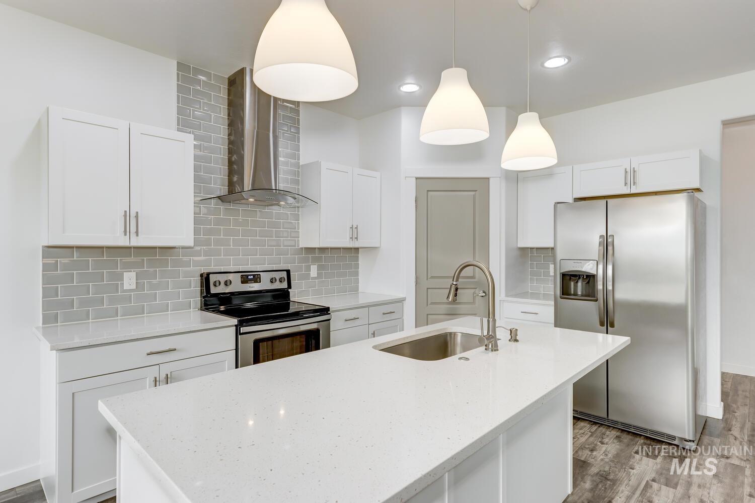 Kitchen with stainless steel appliances, decorative backsplash, wall chimney range hood, light wood-style floors, and a kitchen island with sink