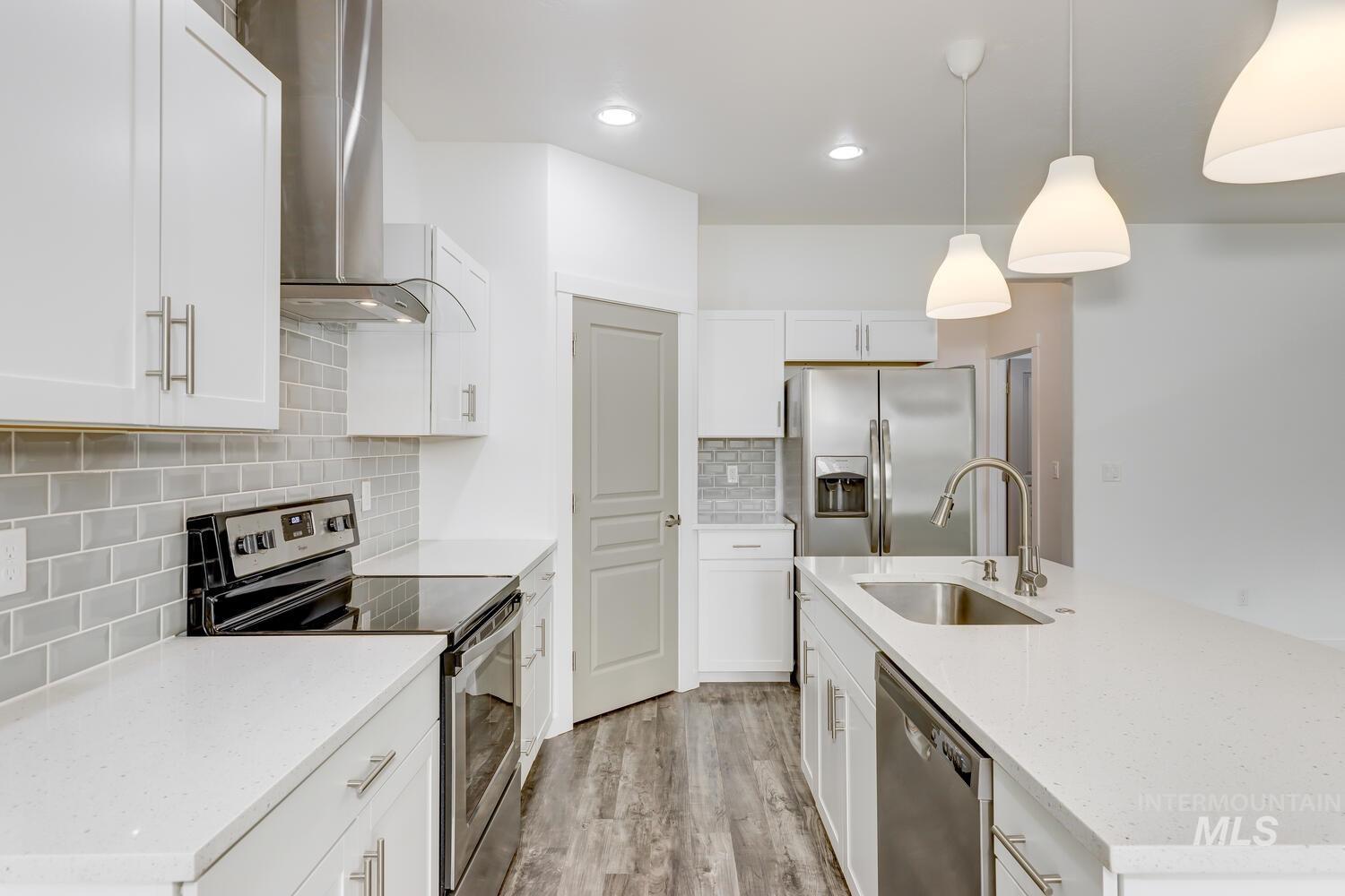 Kitchen with appliances with stainless steel finishes, wall chimney range hood, tasteful backsplash, an island with sink, and white cabinetry