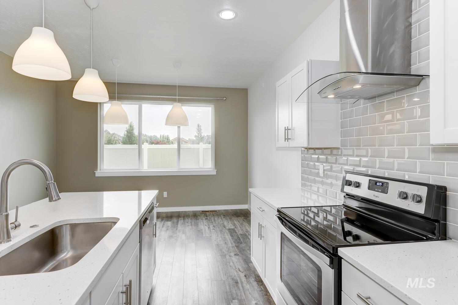 Kitchen with appliances with stainless steel finishes, wall chimney exhaust hood, light wood-style flooring, light stone countertops, and white cabinets