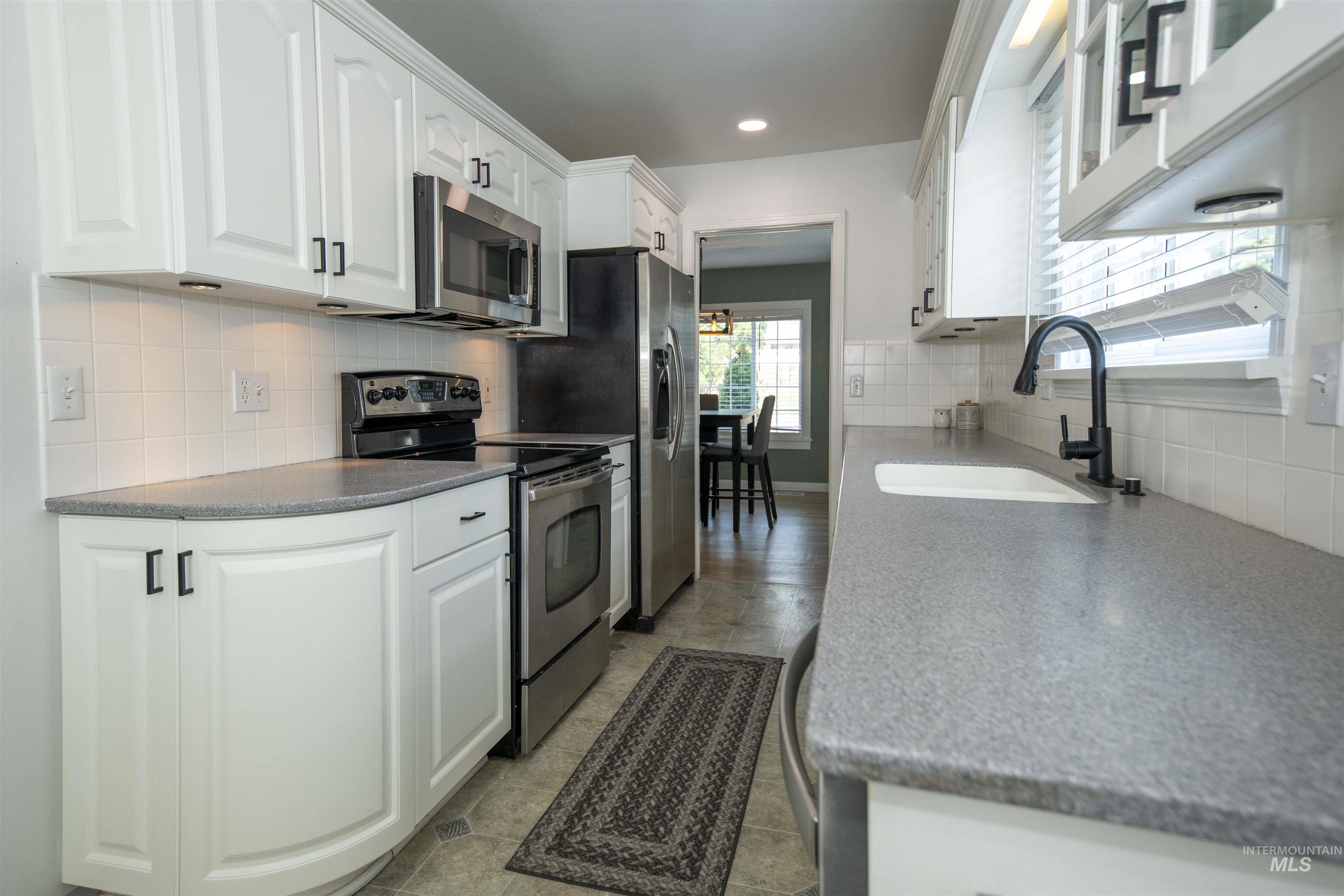 Kitchen with stainless steel appliances, white cabinets, recessed lighting, and decorative backsplash