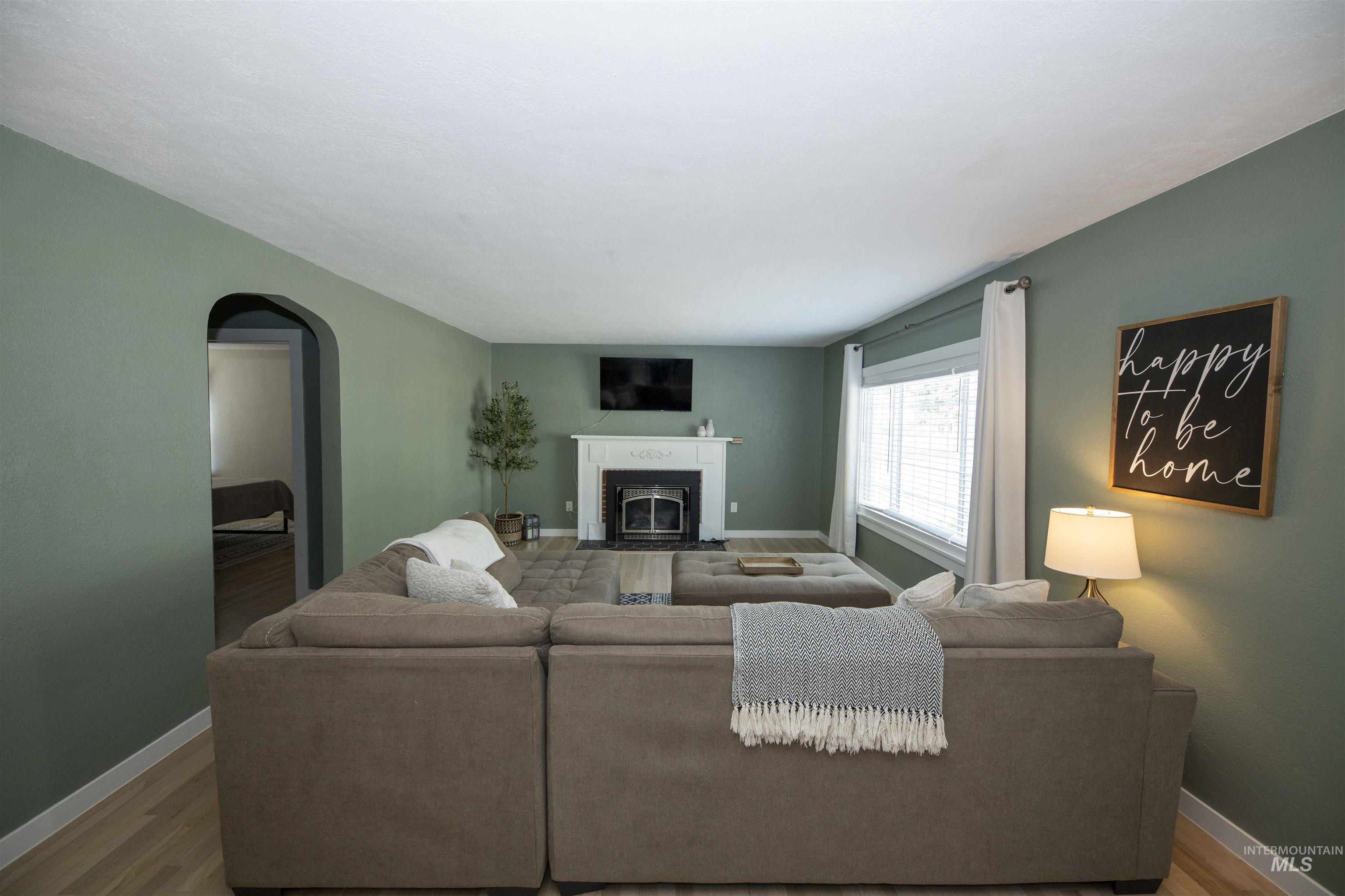 Living room featuring wood finished floors, arched walkways, and a fireplace with flush hearth
