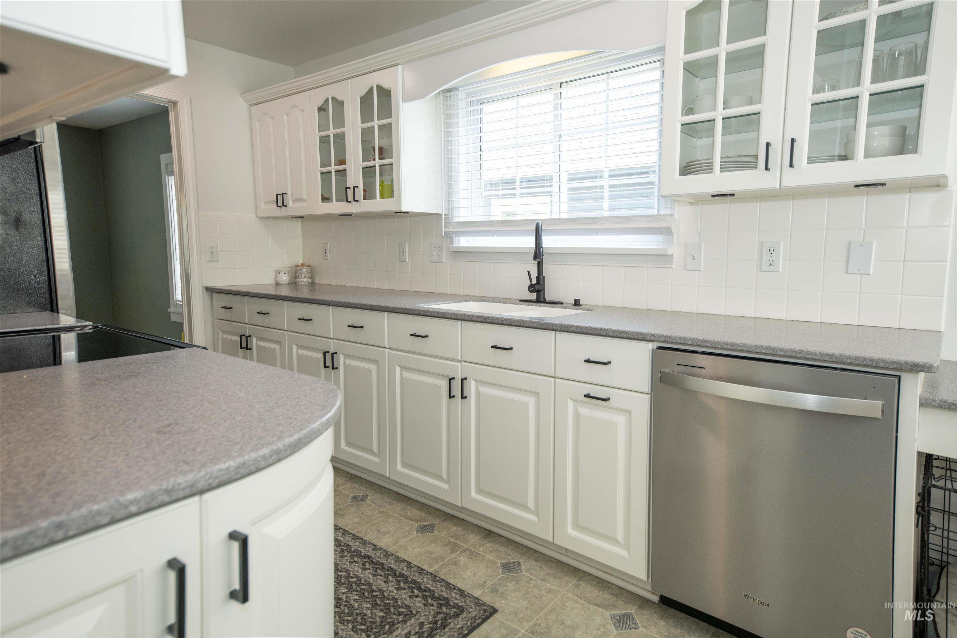 Kitchen with dishwasher, glass insert cabinets, white cabinets, decorative backsplash, and light tile patterned floors