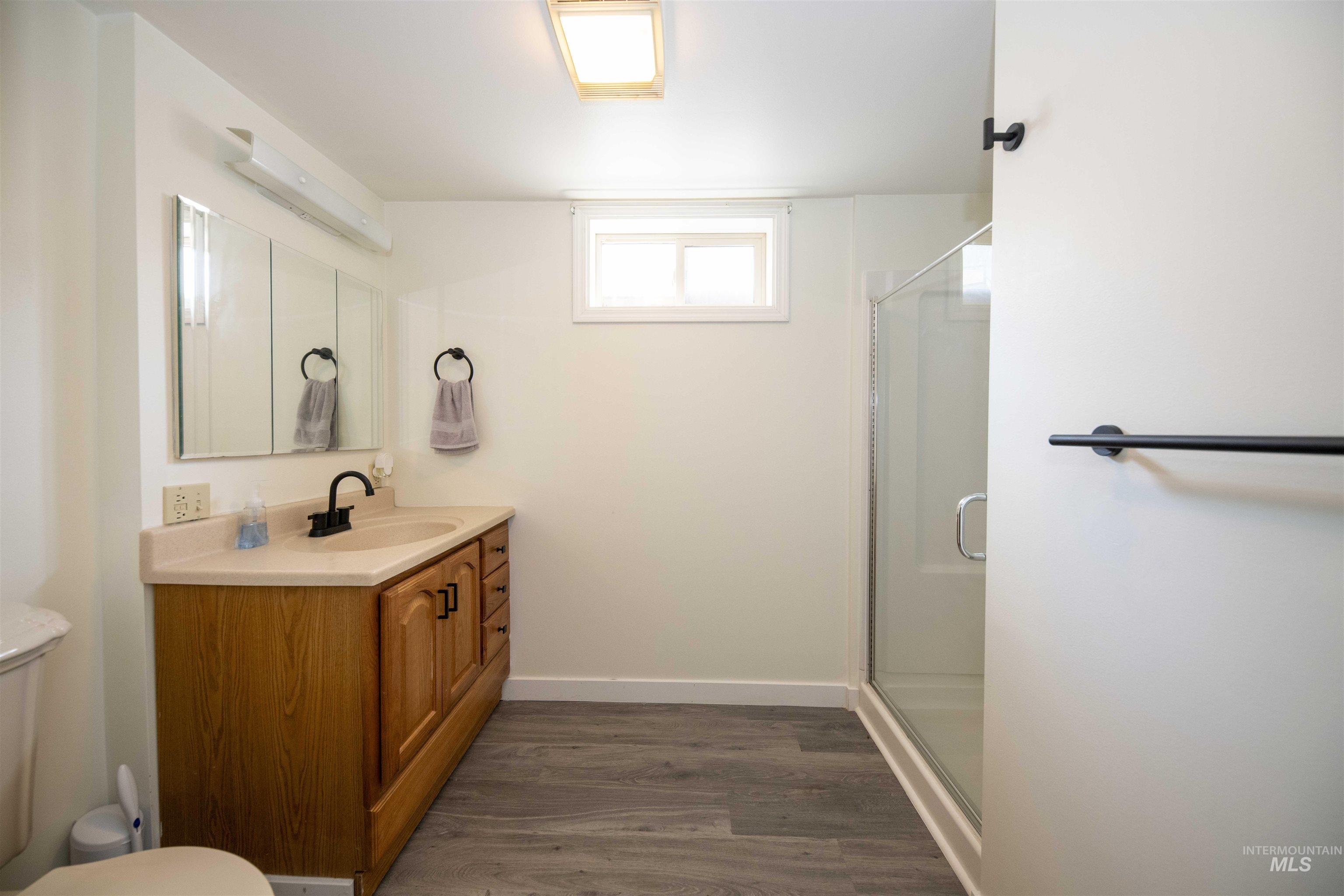 Bathroom in basement of main house - Full bathroom with vanity, wood finished floors, and a stall shower