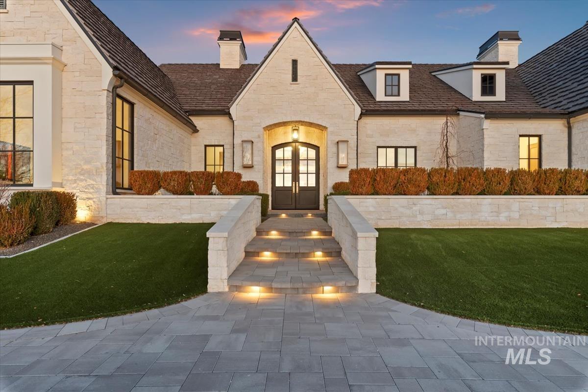 View of front of home with stone siding, french doors, a chimney, and a front lawn