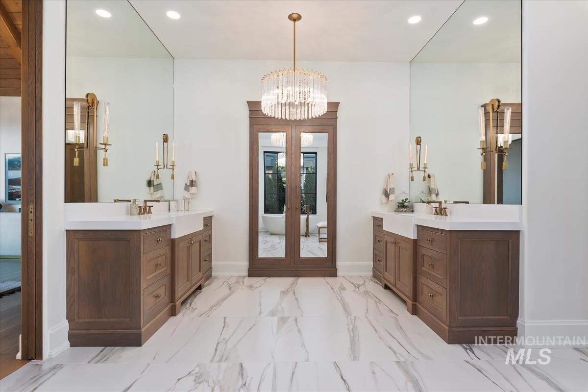 Full bathroom featuring recessed lighting, two vanities, marble look tiles, a chandelier, and a soaking tub