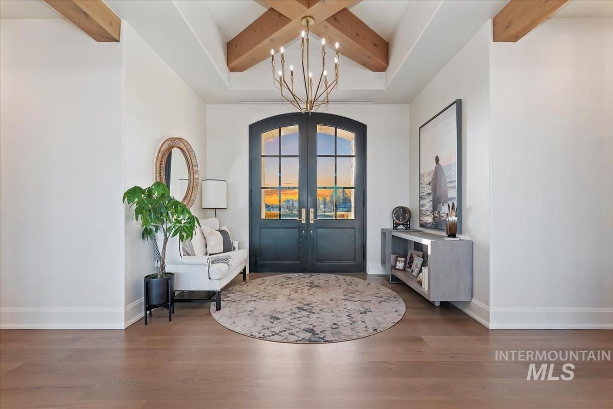 Entrance foyer with a chandelier, french doors, beam ceiling, and wood finished floors