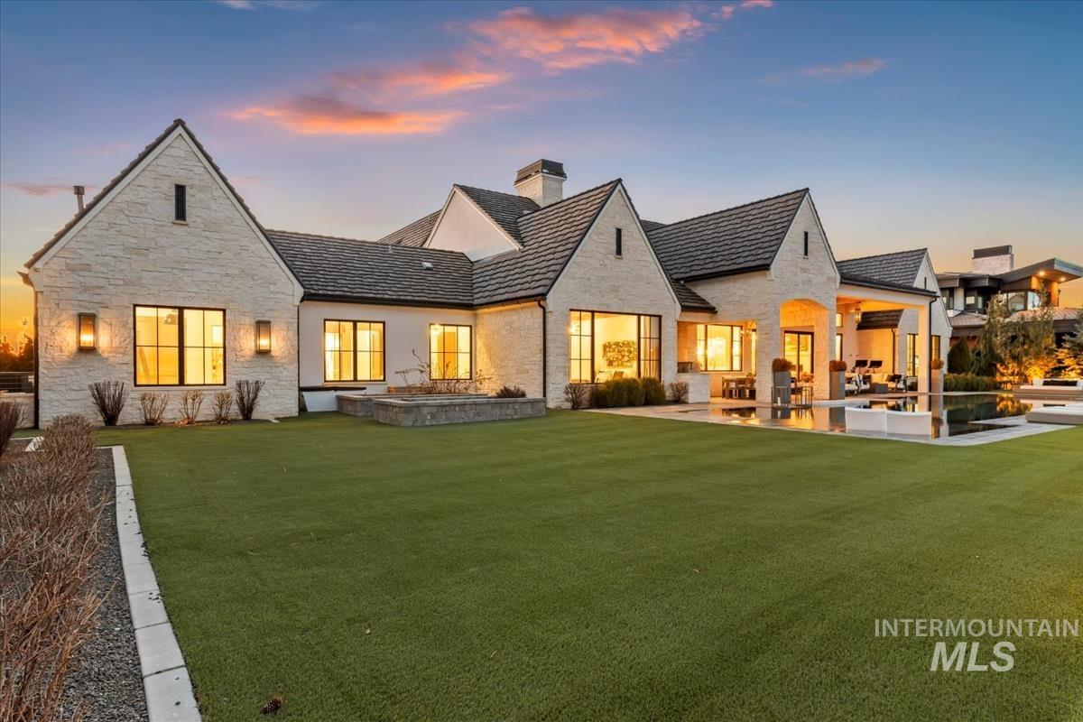 Rear view of property featuring a patio, a chimney, a yard, and stone siding