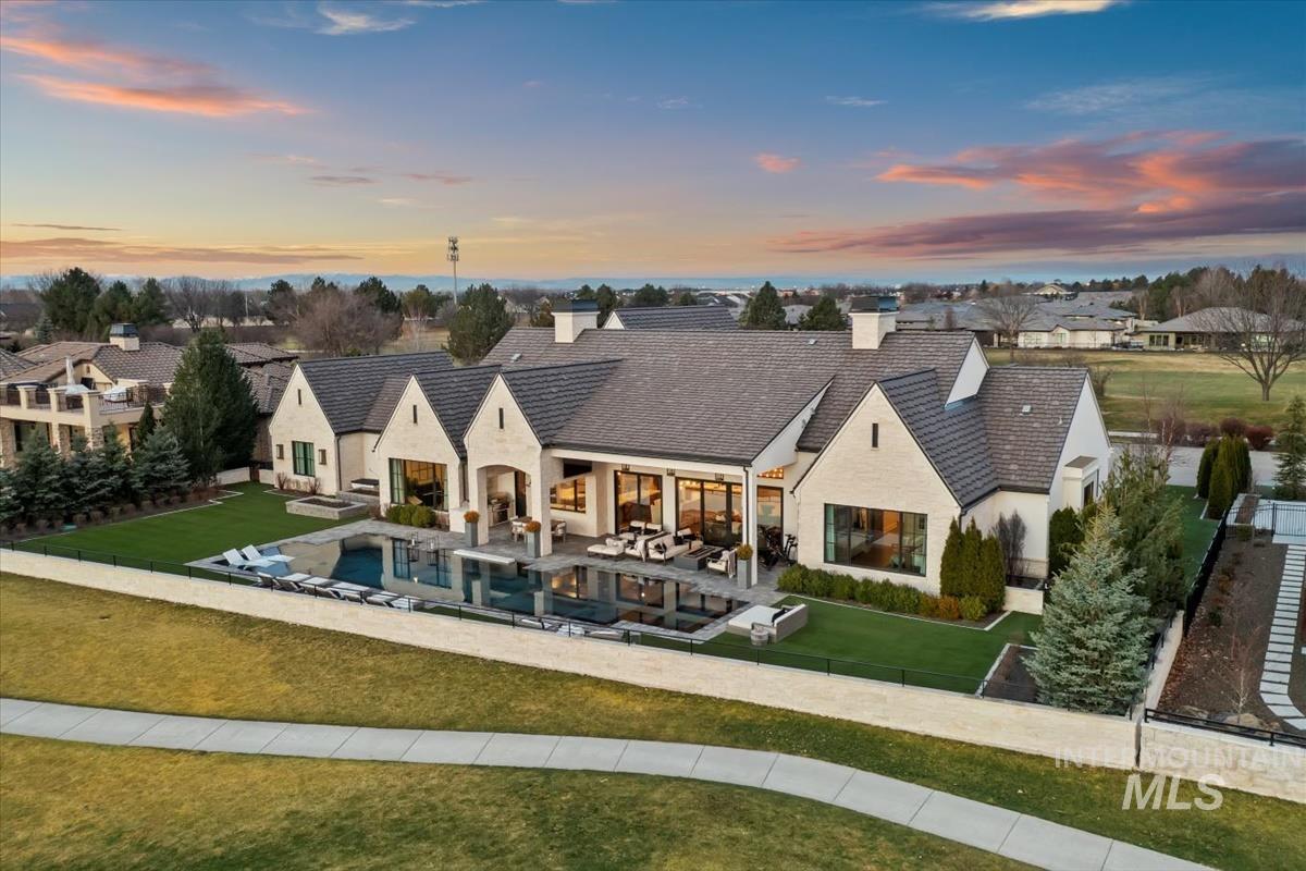 Back of house at dusk with a lawn, an outdoor pool, a patio area, a chimney, and stucco siding