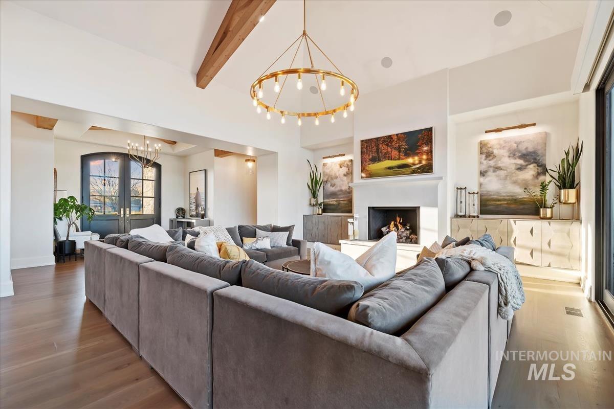 Living room featuring beamed ceiling, a warm lit fireplace, a chandelier, and wood finished floors