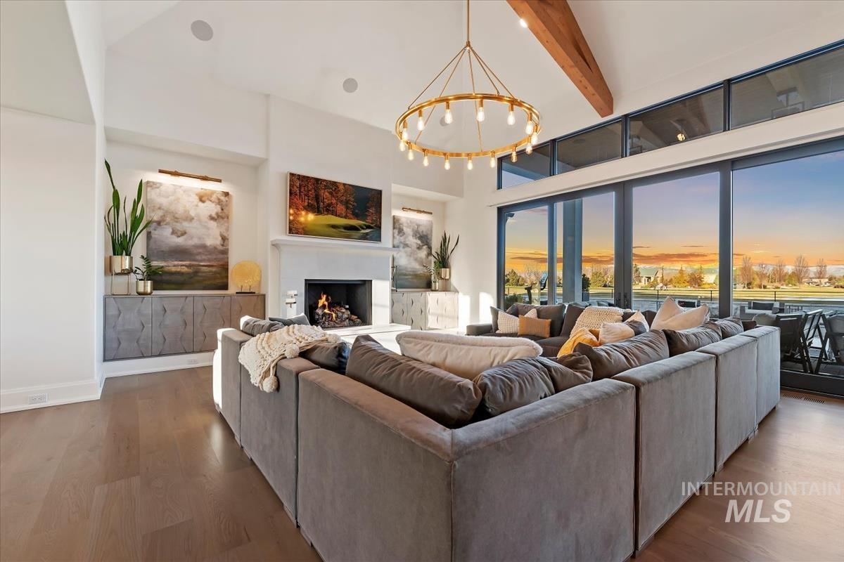 Living room with a warm lit fireplace, beam ceiling, high vaulted ceiling, a chandelier, and wood finished floors