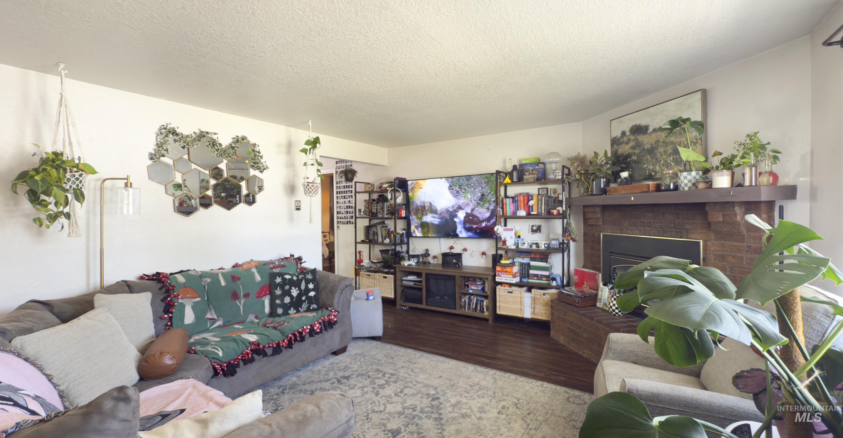 Living area with wood finished floors, a brick fireplace, and a textured ceiling