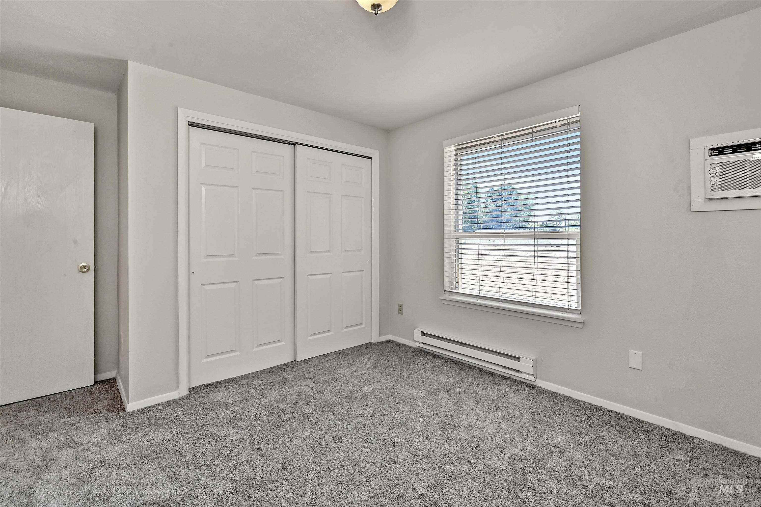 Unit A: Bedroom 2 with a baseboard heating unit, carpet flooring, a closet, and an AC wall unit
