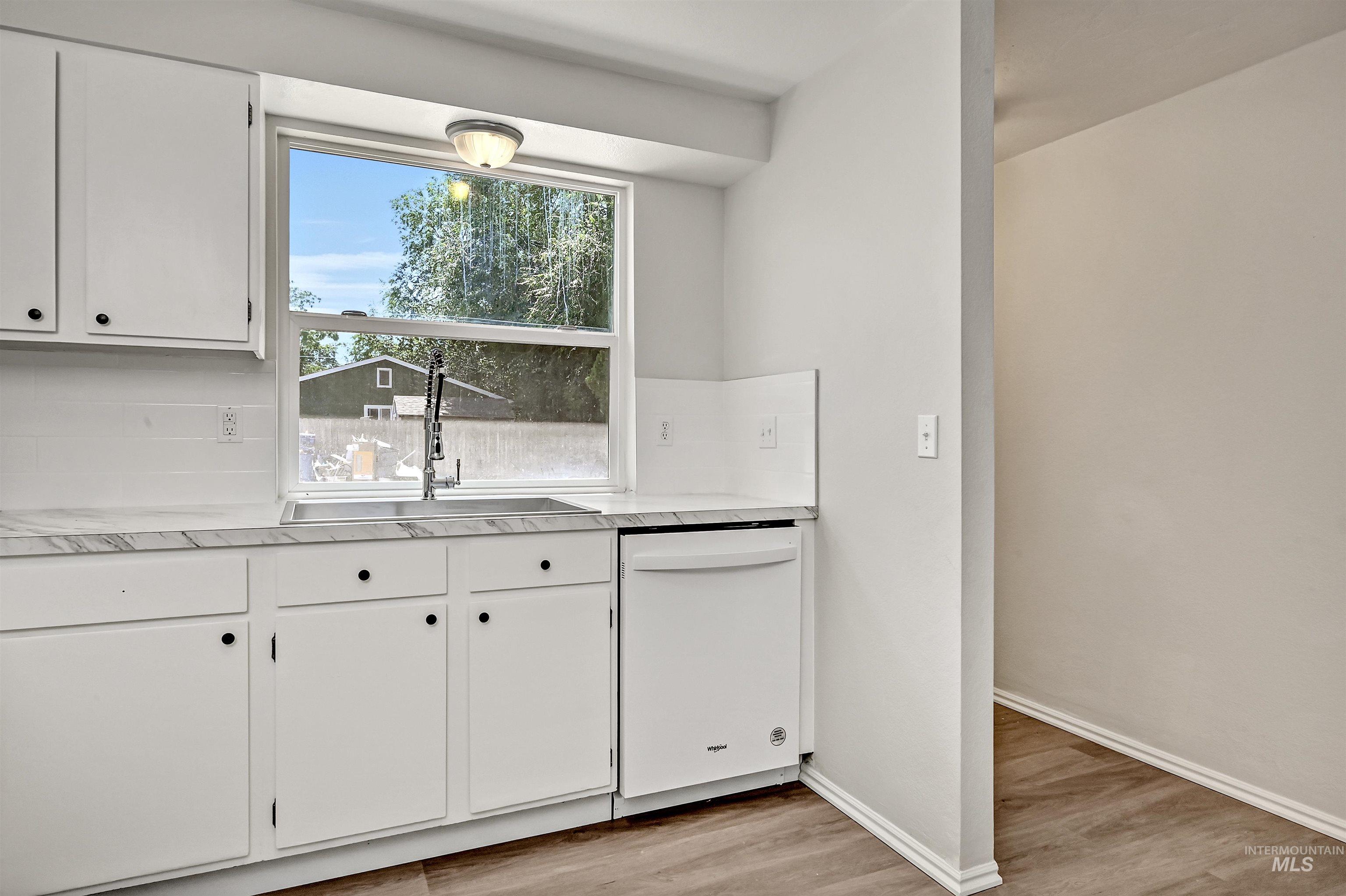 Unit B: Entry and kitchen - featuring dishwasher, light countertops, LVP flooring, and white cabinets