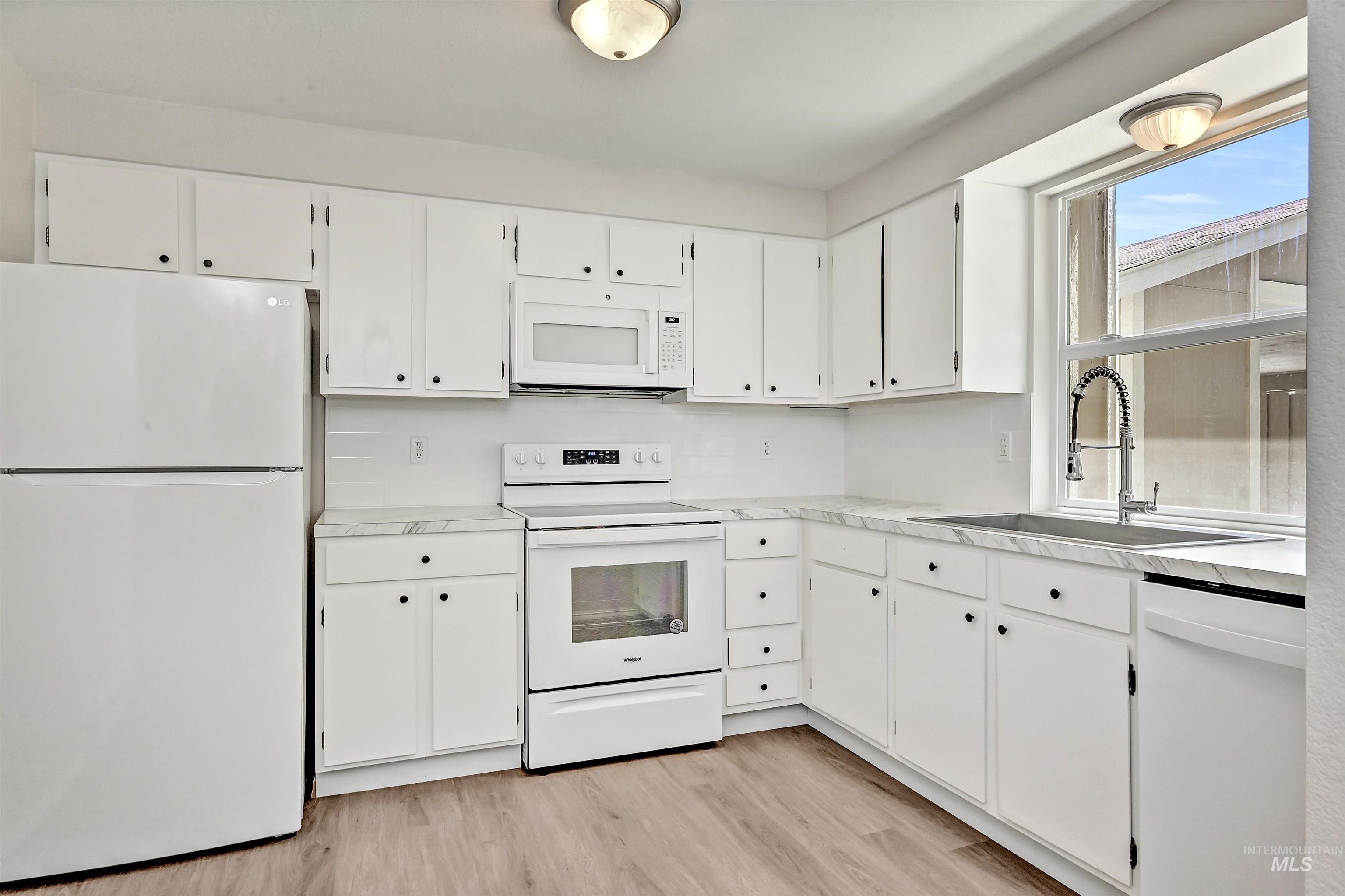Unit B: Kitchen with white appliances, white cabinetry, LVP flooring, and light countertops