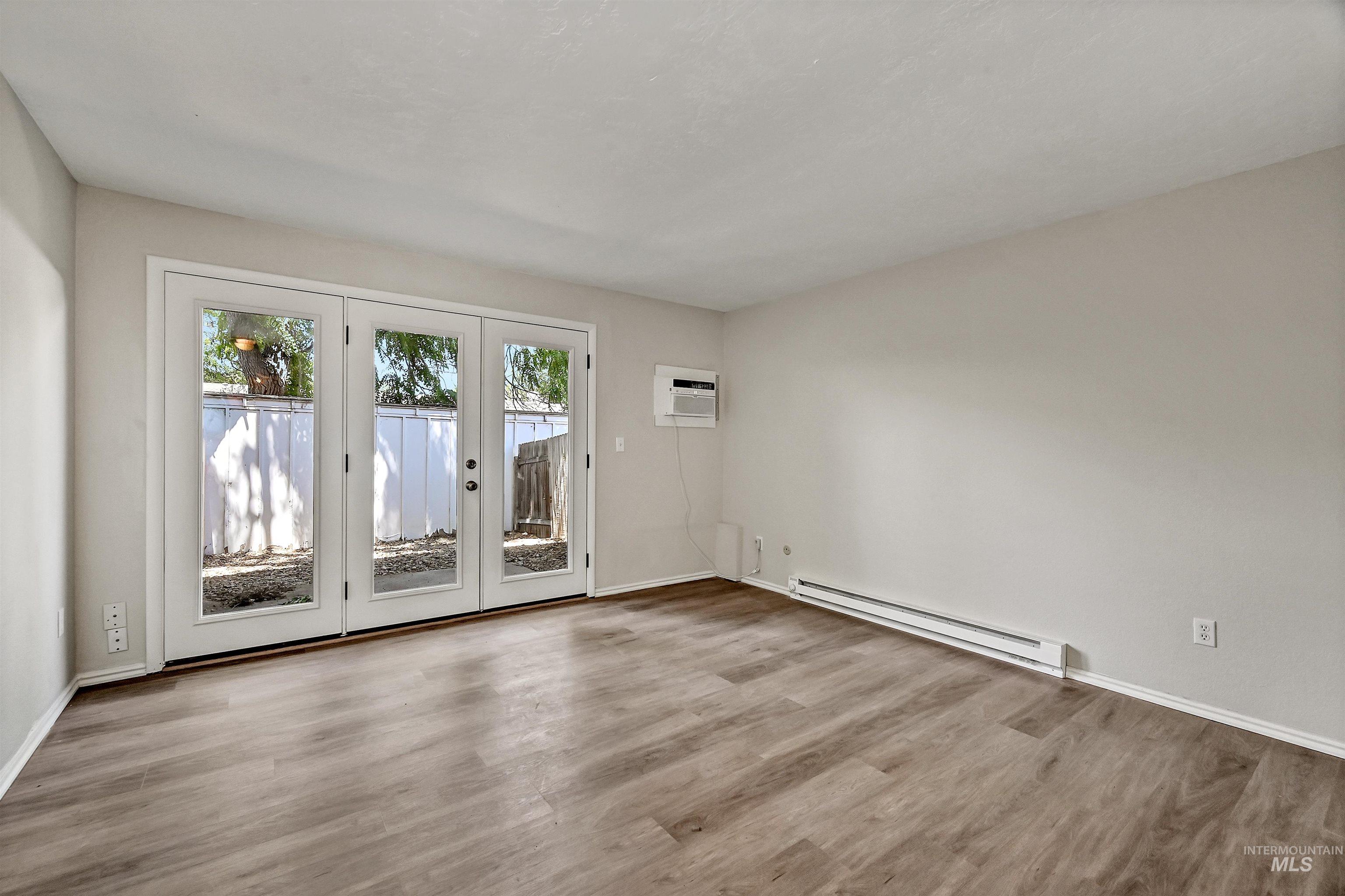 Unit B: Living room with baseboard radiator, LVP flooring, a wall mounted air conditioner, and door to patio/yard.
