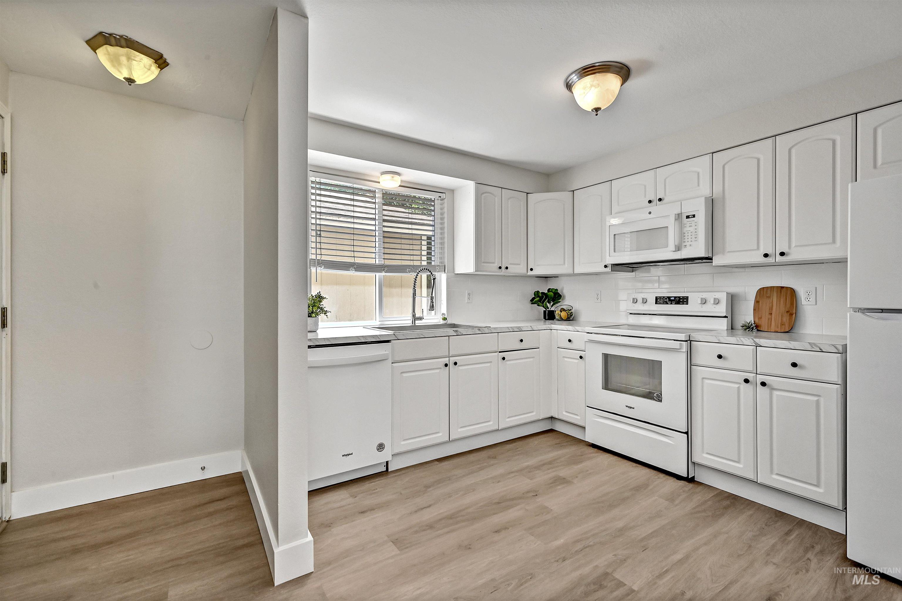 Unit A: Kitchen with white appliances, LVP flooring, white cabinetry, and light countertops