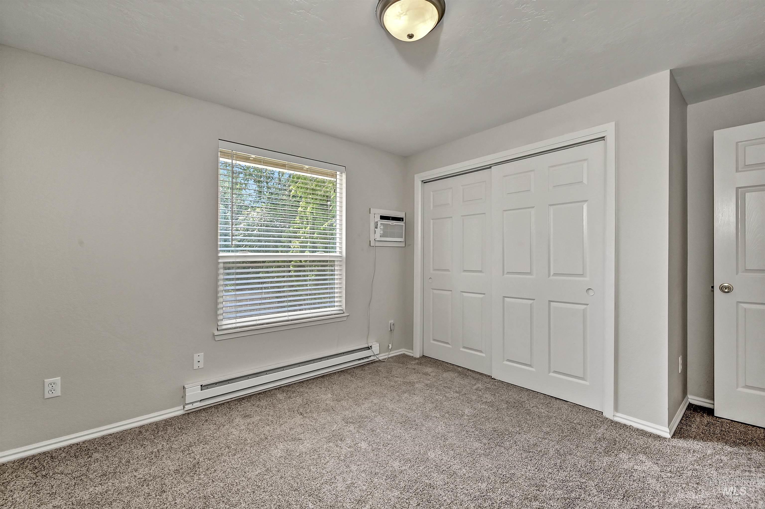 Unit B: Bedroom 2 with a baseboard radiator, carpet flooring, a closet, and a wall mounted AC