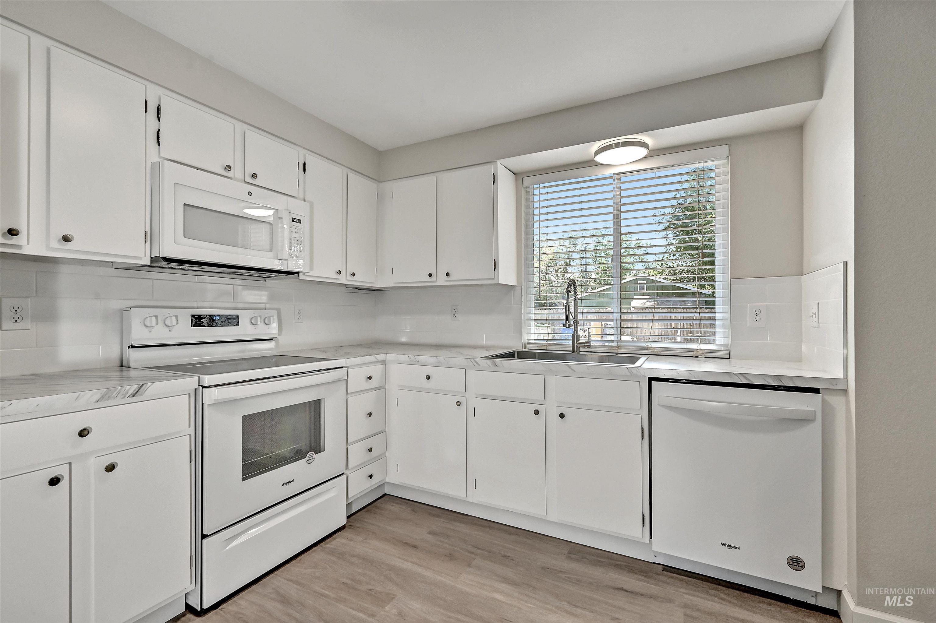 Unit C: Kitchen featuring white appliances, LVP flooring, white cabinetry, light countertops, and decorative backsplash