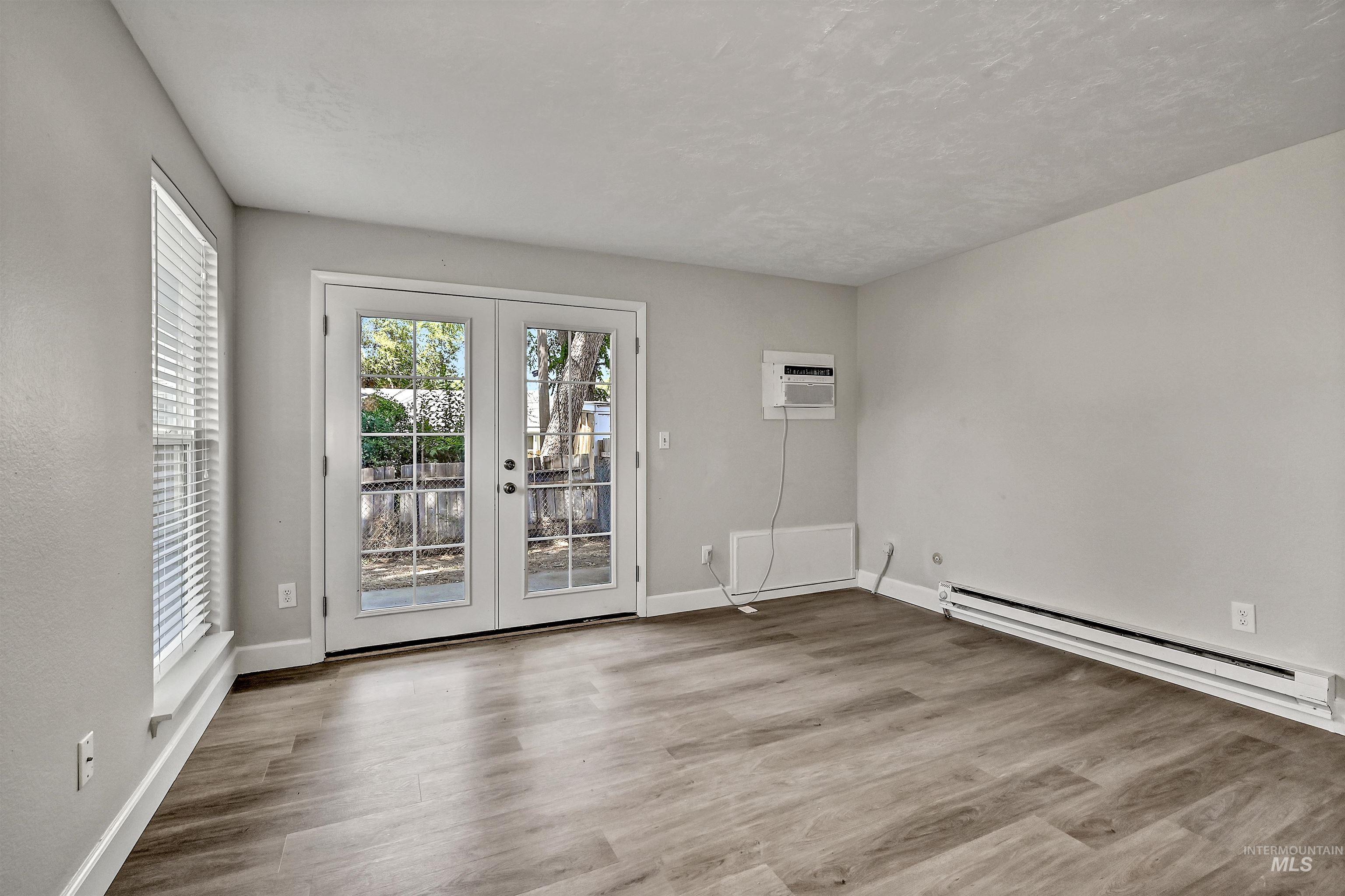 Unit C: Living room featuring french doors, baseboard heating, LVP flooring, a wall mounted AC, and a textured ceiling