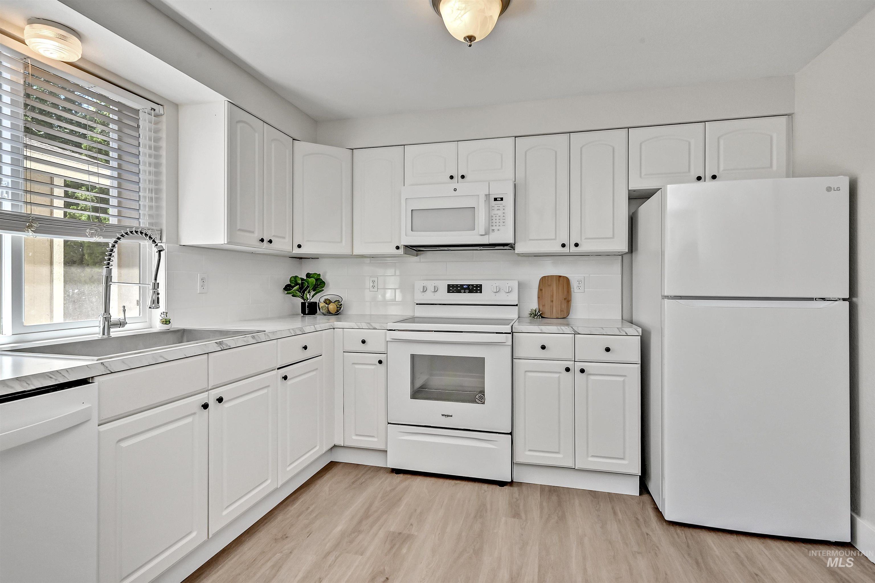 Kitchen with white appliances, LVP flooring, white cabinets, light countertops, and tasteful backsplash