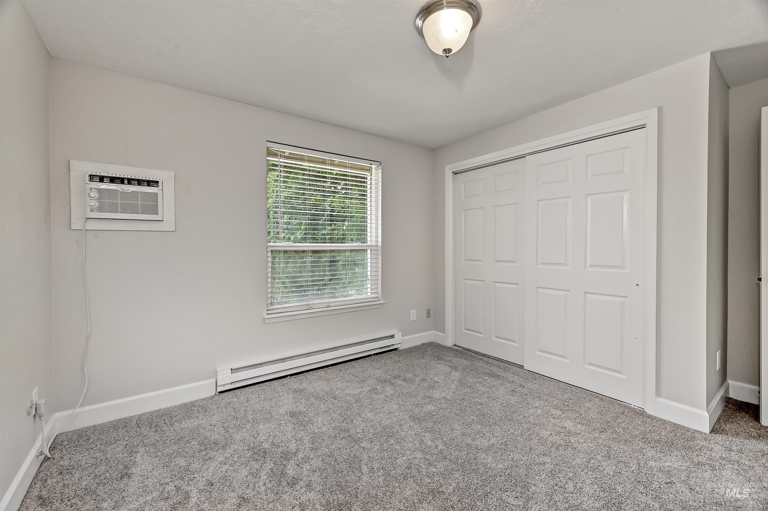 Unit C: Bedroom 1 featuring a baseboard radiator, carpet, a closet, and a wall mounted air conditioner