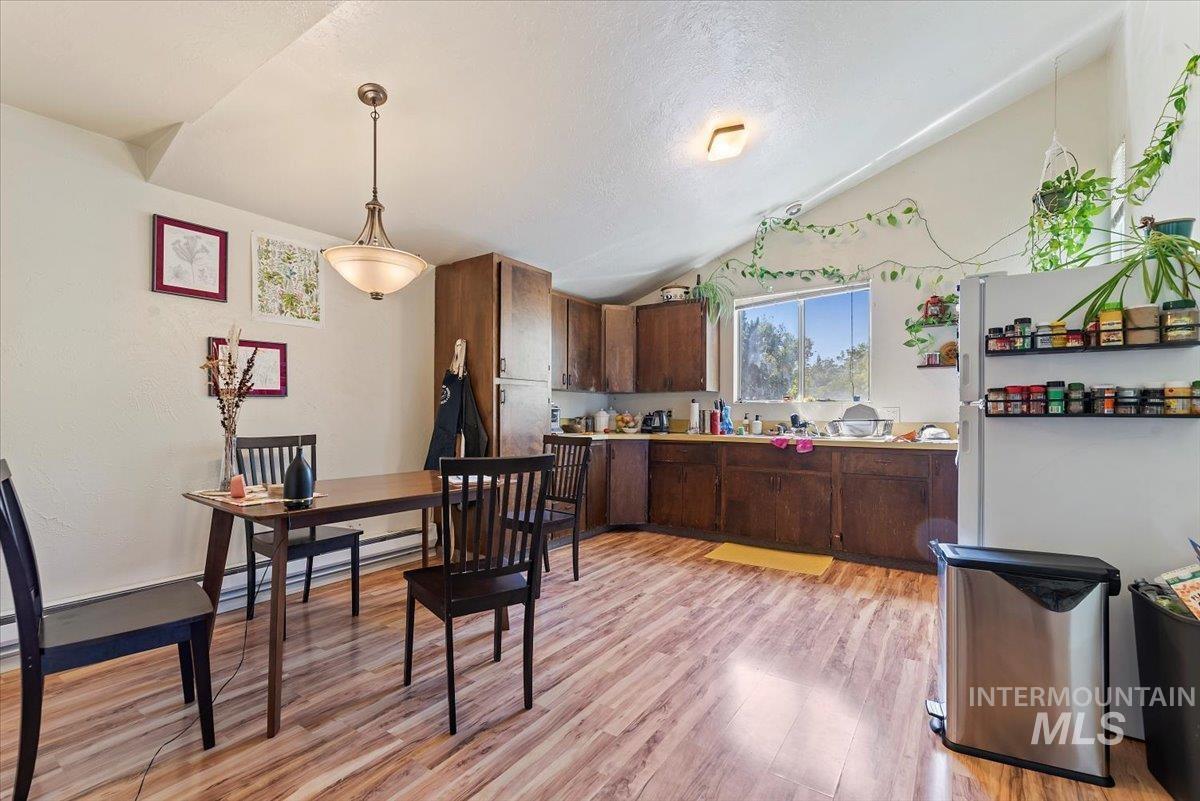 Kitchen featuring light wood-style flooring, light countertops, vaulted ceiling, freestanding refrigerator, and pendant lighting