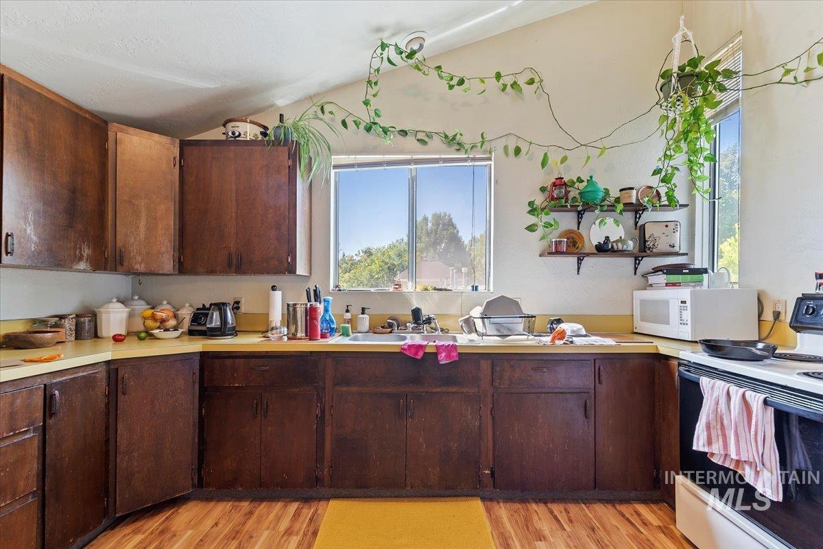 Kitchen featuring white appliances, light wood-style floors, light countertops, and lofted ceiling