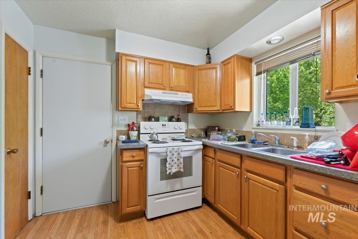 Kitchen with white range with electric stovetop, light wood-style floors, under cabinet range hood, tasteful backsplash, and a textured ceiling
