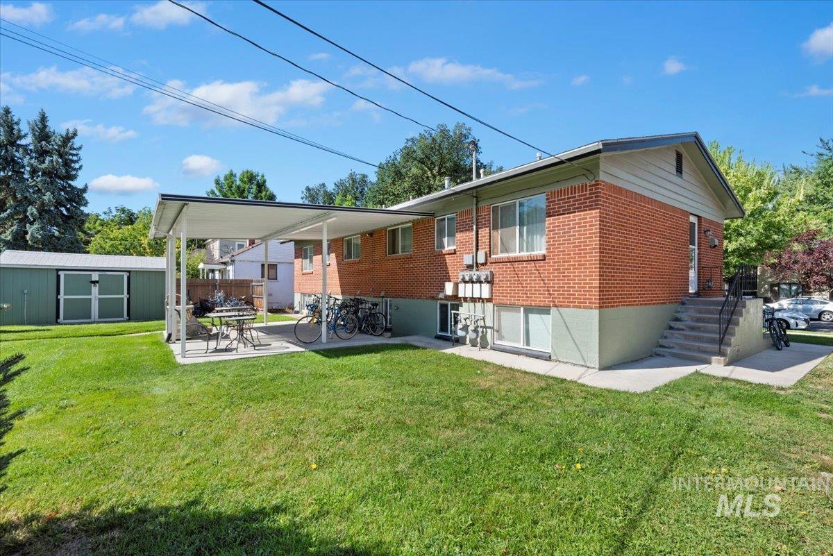 Back of house with a yard, brick siding, a patio, and a shed