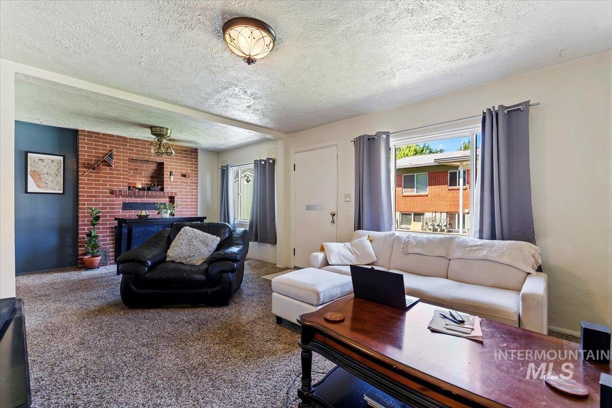 Carpeted living room featuring a textured ceiling, an office area, and a brick fireplace