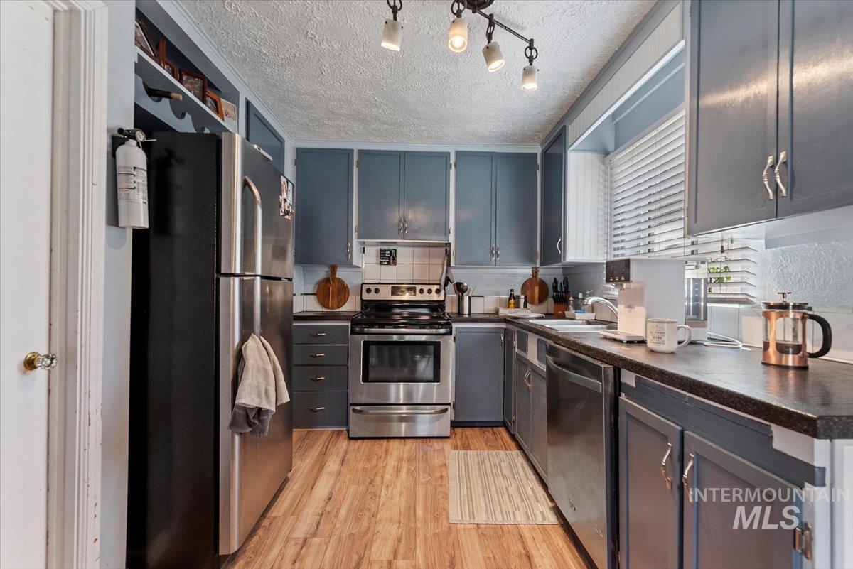Kitchen featuring dark countertops, light wood finished floors, stainless steel appliances, and a textured ceiling