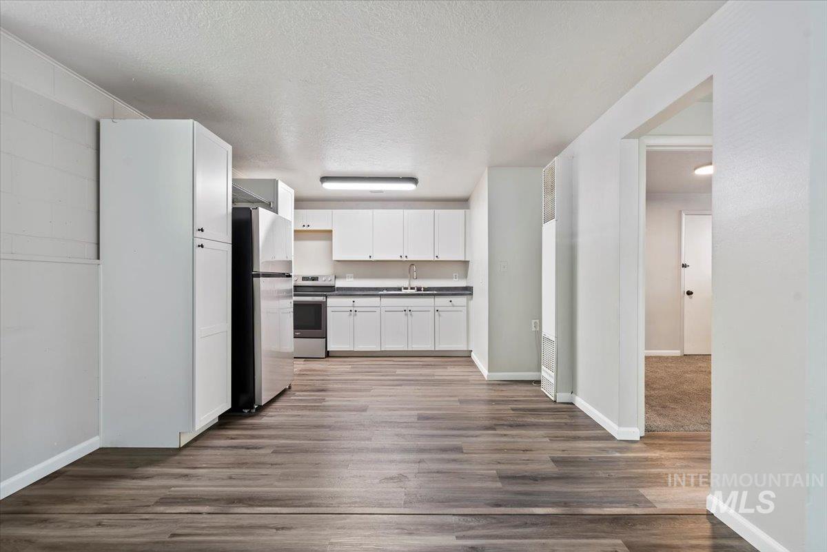 Kitchen with dark countertops, a textured ceiling, white cabinets, freestanding refrigerator, and wood finished floors