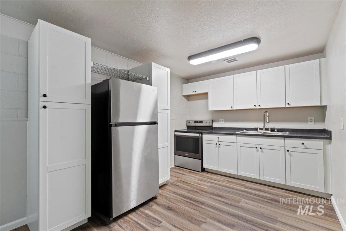 Kitchen featuring stainless steel appliances, light wood-style floors, dark countertops, white cabinets, and a textured ceiling