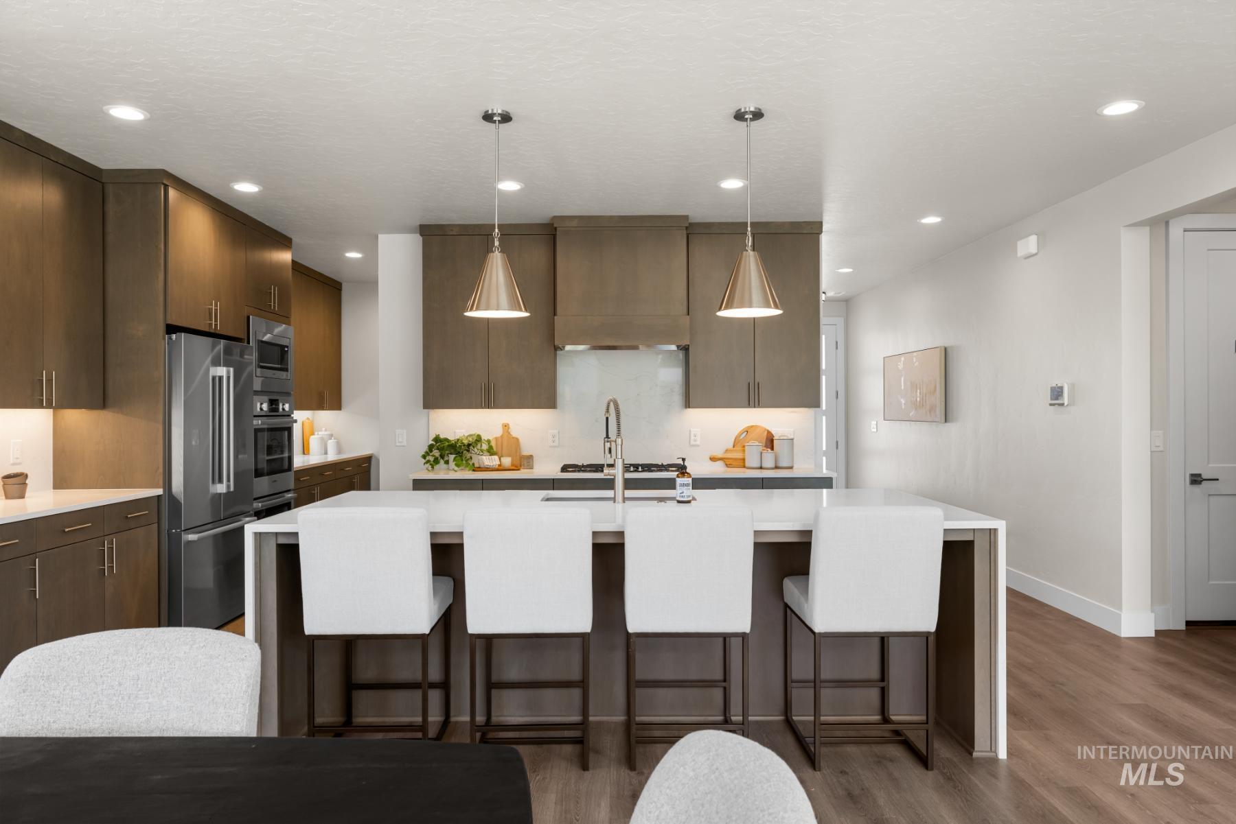 Kitchen featuring light countertops, stainless steel appliances, dark wood-type flooring, recessed lighting, and a breakfast bar area