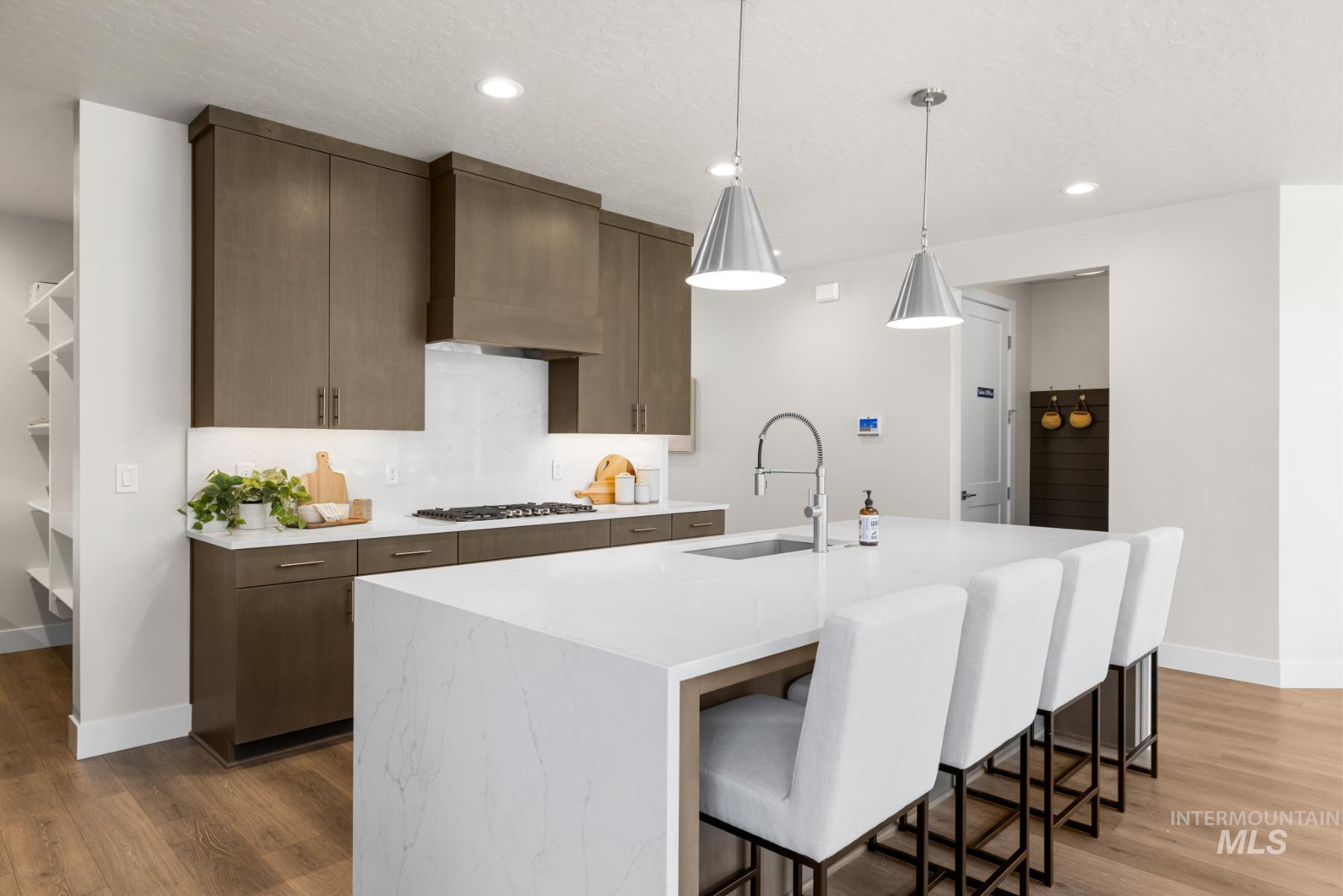 Kitchen with light countertops, light wood finished floors, a breakfast bar area, an island with sink, and recessed lighting