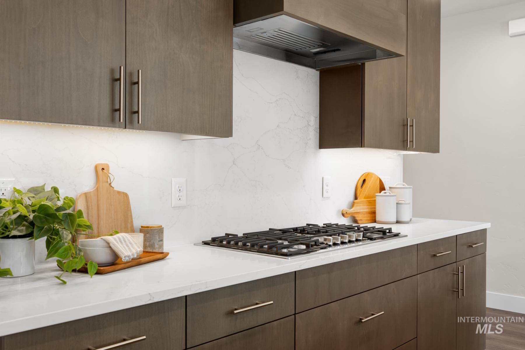 Kitchen with custom exhaust hood, light countertops, dark wood finished floors, stainless steel gas cooktop, and backsplash