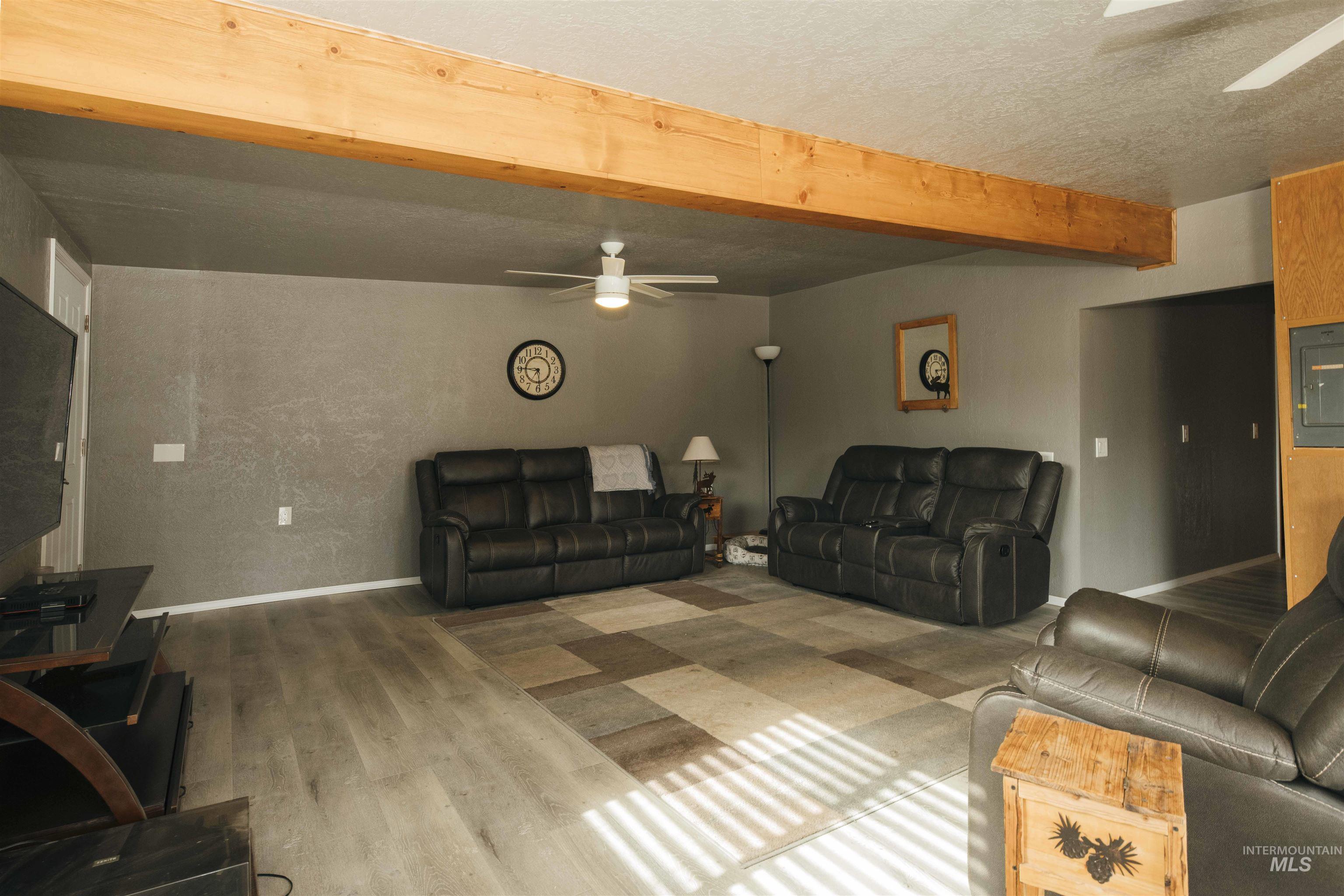 Living room with ceiling fan, beamed ceiling, wood finished floors, electric panel, and a textured ceiling
