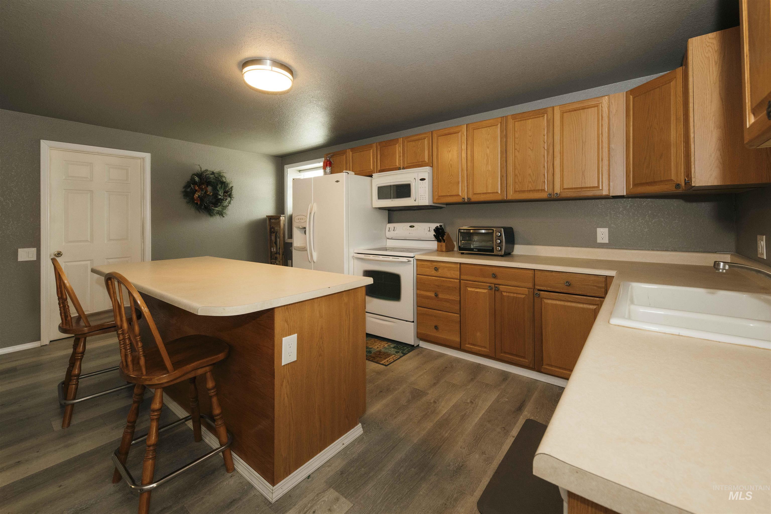 Kitchen featuring white appliances, a kitchen bar, dark wood-type flooring, light countertops, and a kitchen island